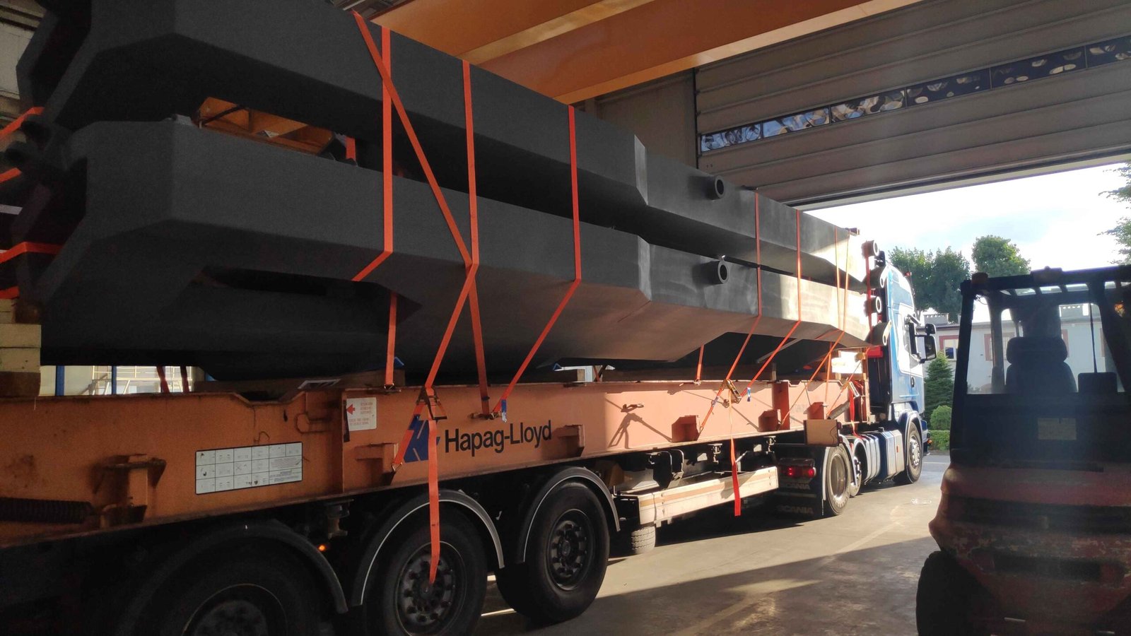 Steel structures secured with lashing straps on a flat-rack container on a road chassis